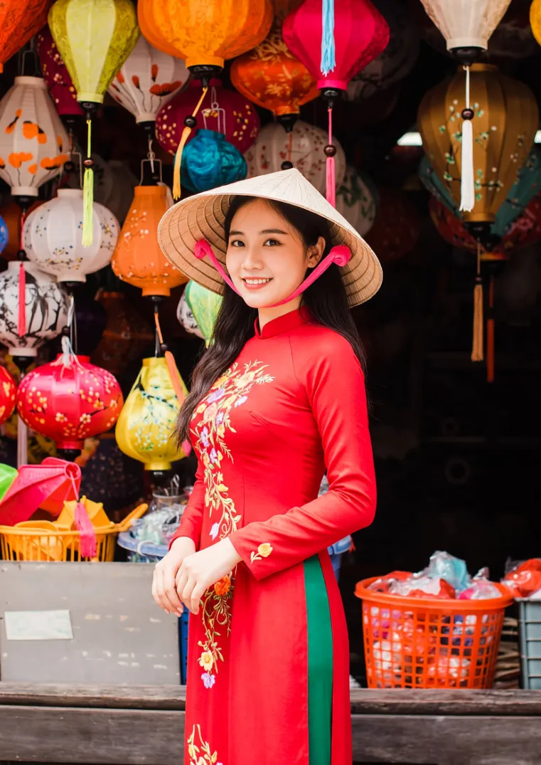 Vietnamese woman in red ao dai and conical hat in front of colourful Hoi An lanterns