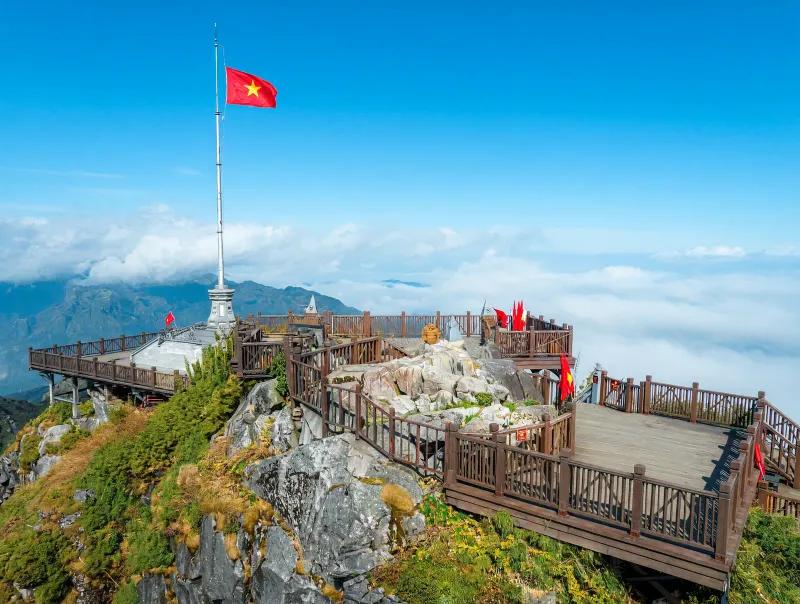 Vietnamese flag flying above the Fansipan summit viewing platform in Sapa, with clouds rolling beneath the boardwalk