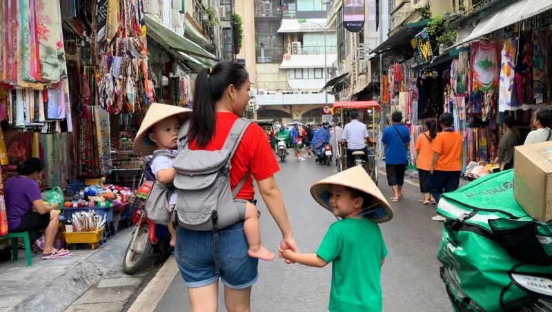 Mother carrying a baby and holding her child's hand while walking through a colourful Ho Chi Minh City market lane