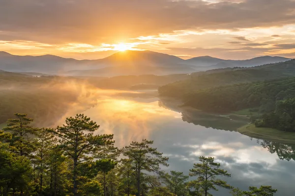 Golden sunrise over a misty lake and pine forested hills in Da Lat, Vietnam's central highlands